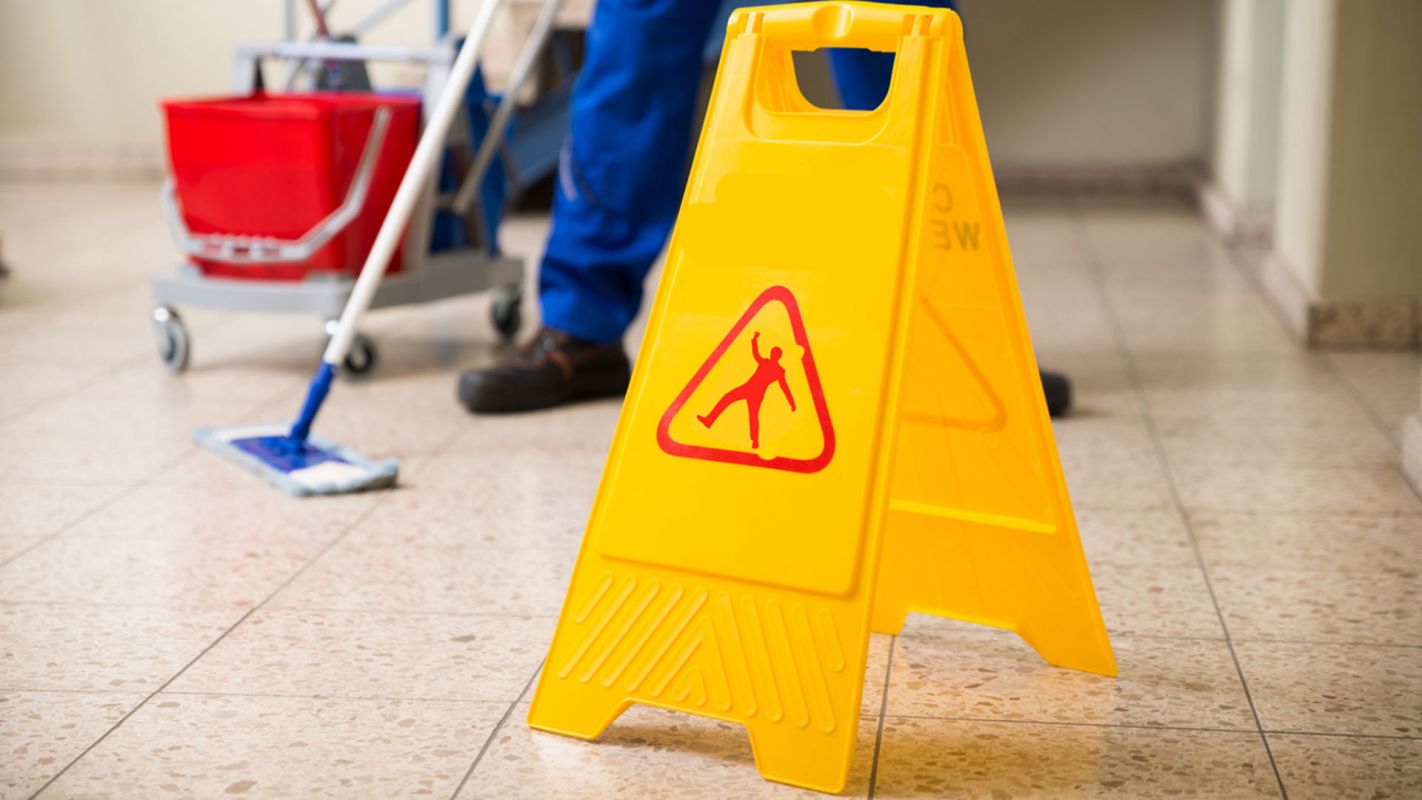 person cleaning floor behind caution sign